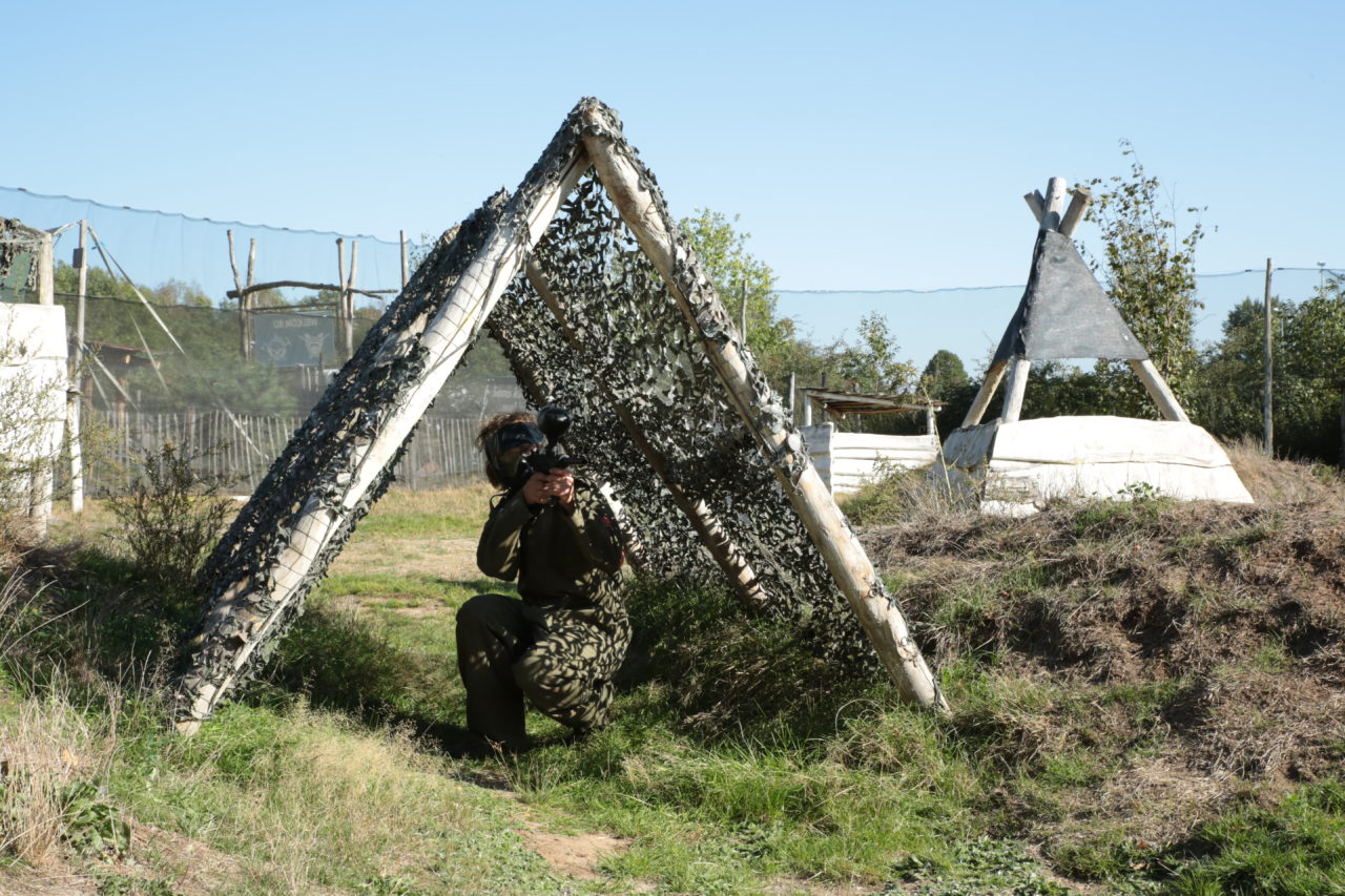 Paintballer verstopt zich onder een camouflagedoek