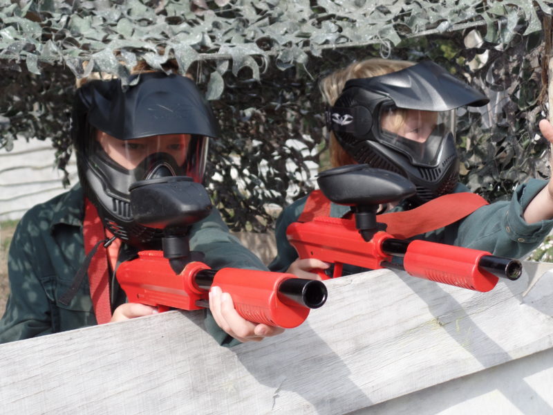 Twee kinderen spelen kinderpaintball en zitten naast elkaar in dekking achter een hindernis